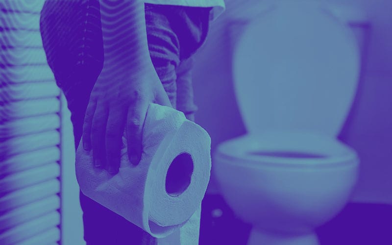 Pessoa que segura um rolo de papel higiénico na casa de banho