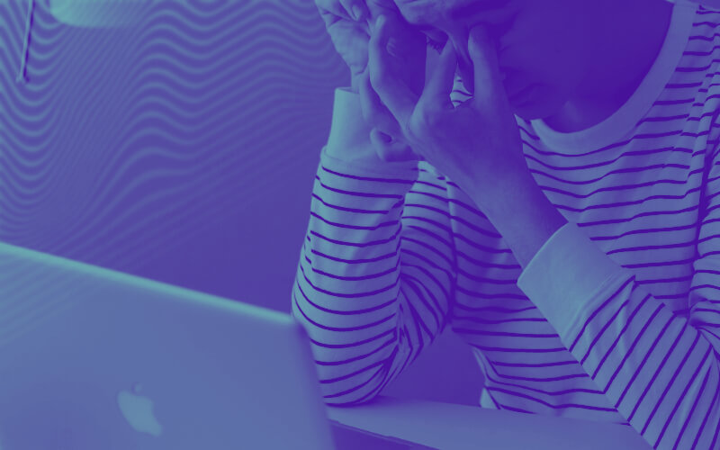 Uma pessoa é com um laptop, cobrindo o rosto com a face em sinal de cansaço