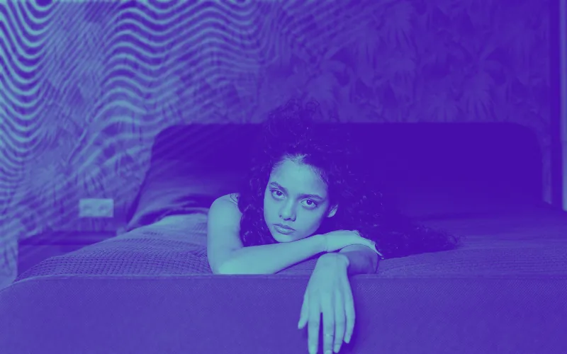 Mulher deitada em cima da cama com ar triste e pensativo