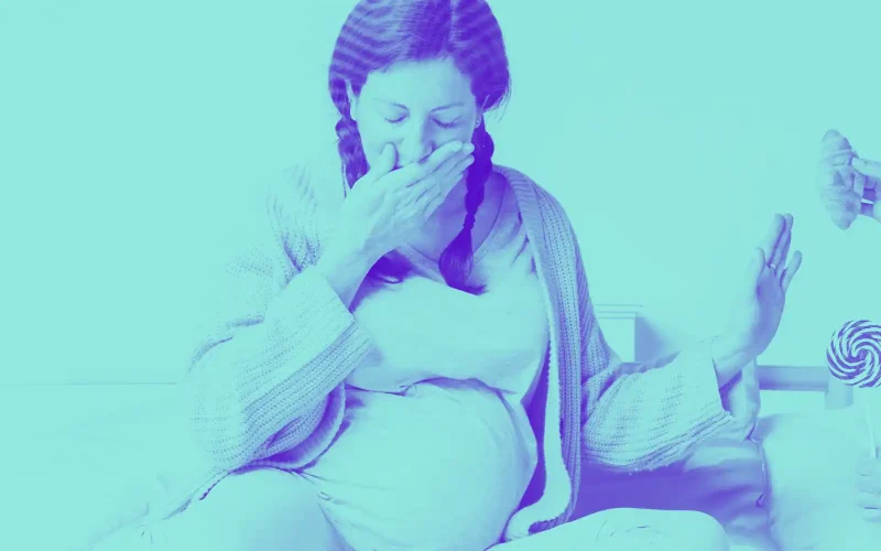 Imagem de mulher grávida recusando comida com aparente sensação de enjoo ou náusea